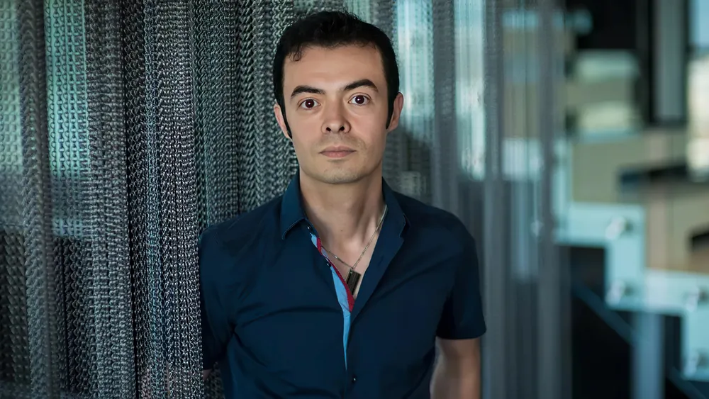 Orkut Buyukkokten, fundador do Orkut, em pé com camisa azul diante de uma tela de malha.
